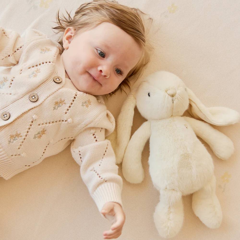 Baby laying against floor with light yellow coloured Jamie Kay bunny soft toy.