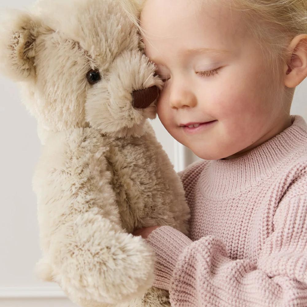 Toddler holding beige Jamie kay teddy bear against white background.