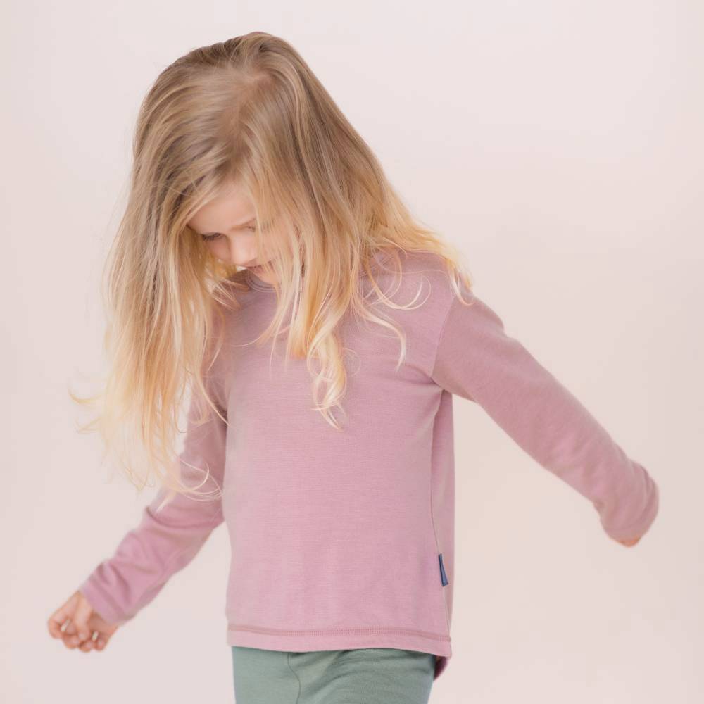 Child wearing a merino pink long-sleeve shirt on a plain background