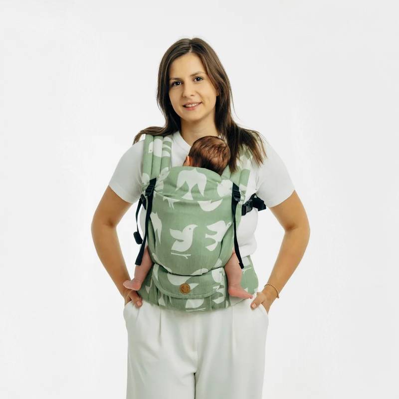 A woman wearing a green baby carrier with white birds on it and a baby inside. 