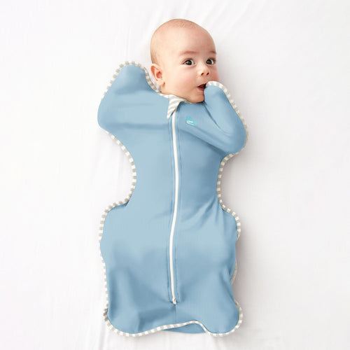 A baby wrapped in a light blue zippered swaddle blanket lying on a white background.