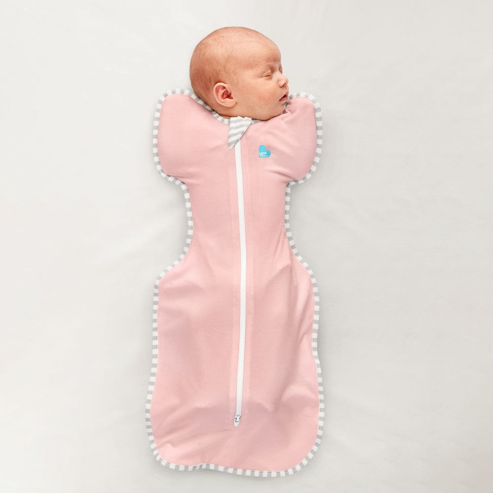 Newborn baby sleeping in a pink swaddle with white trim on a light gray background