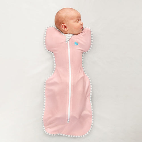 Newborn baby sleeping in a pink swaddle with white trim on a light gray background