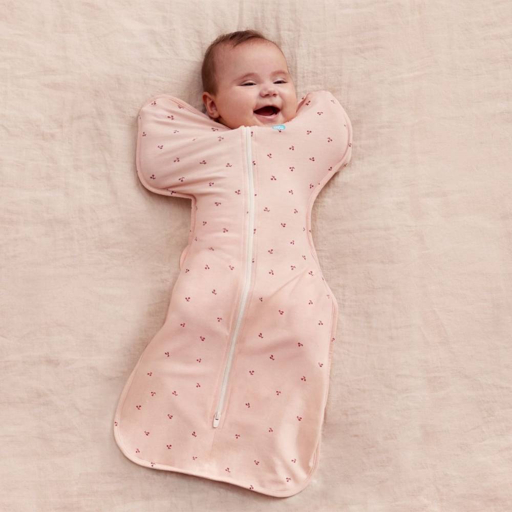 Baby in a pink sleep swaddle with a subtle pattern on a soft beige background