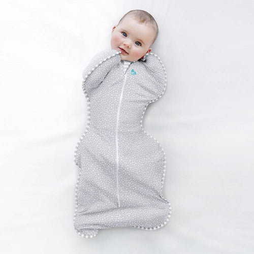 Baby wrapped in a gray swaddle with white polka dots on a light gray background