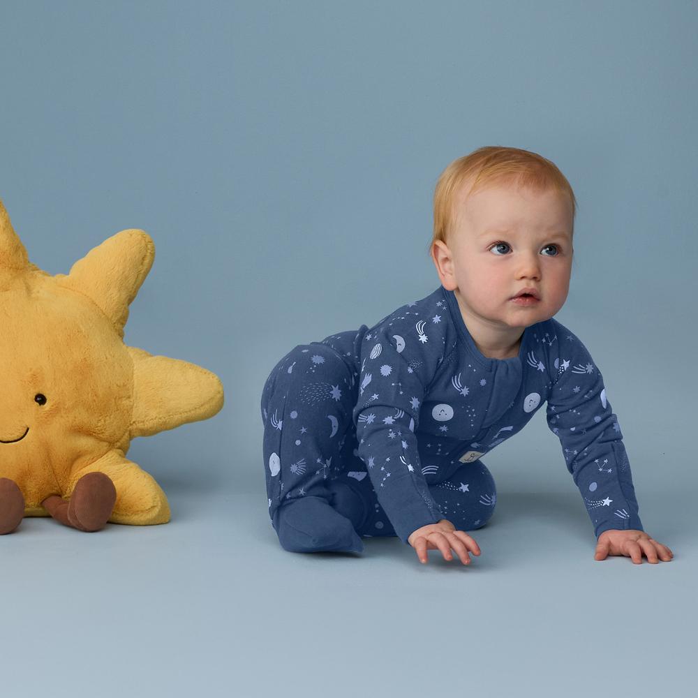 Baby in a blue onesie with star pattern crawling next to a yellow plush toy on a blue background