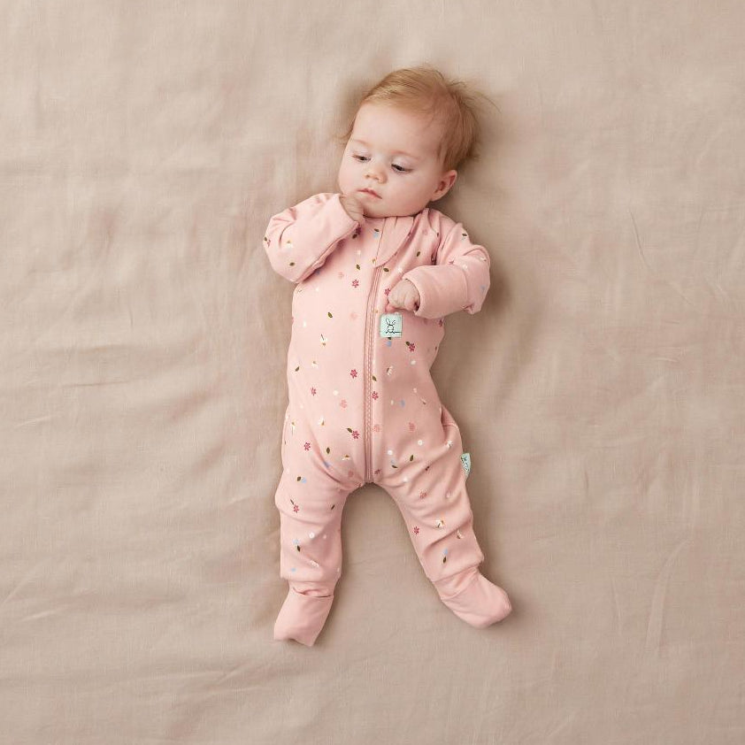Baby in a pink onesie lying on a beige blanket