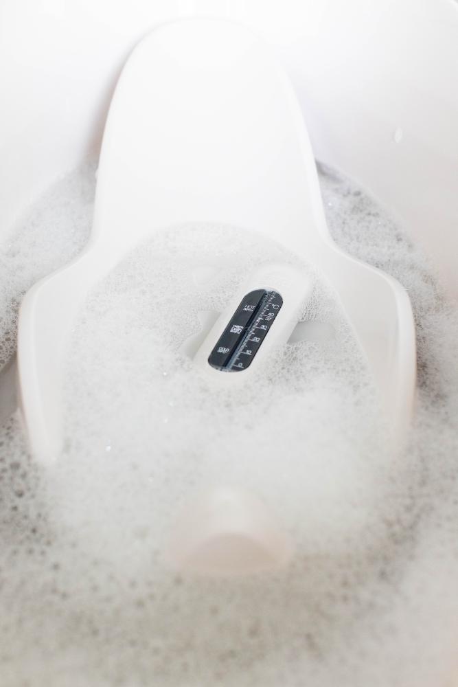 White LUMA Bath Thermometer in a baby bath with water and bubbles. 