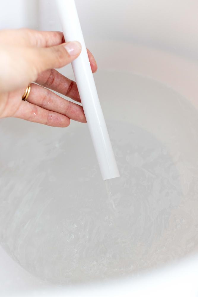 A hand holding a LUMA bath drain tube, while it is draining water out. 