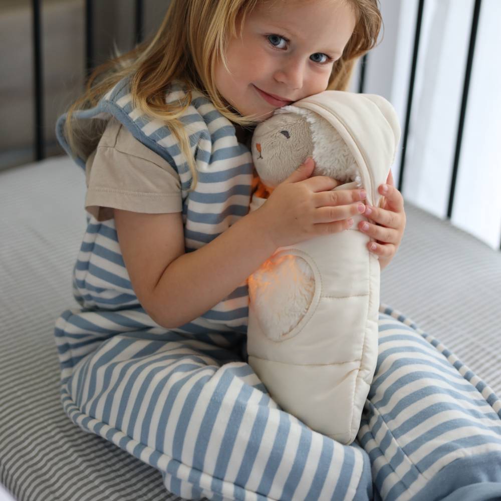 Child in striped pajamas holding a glowing plush toy on a bed.