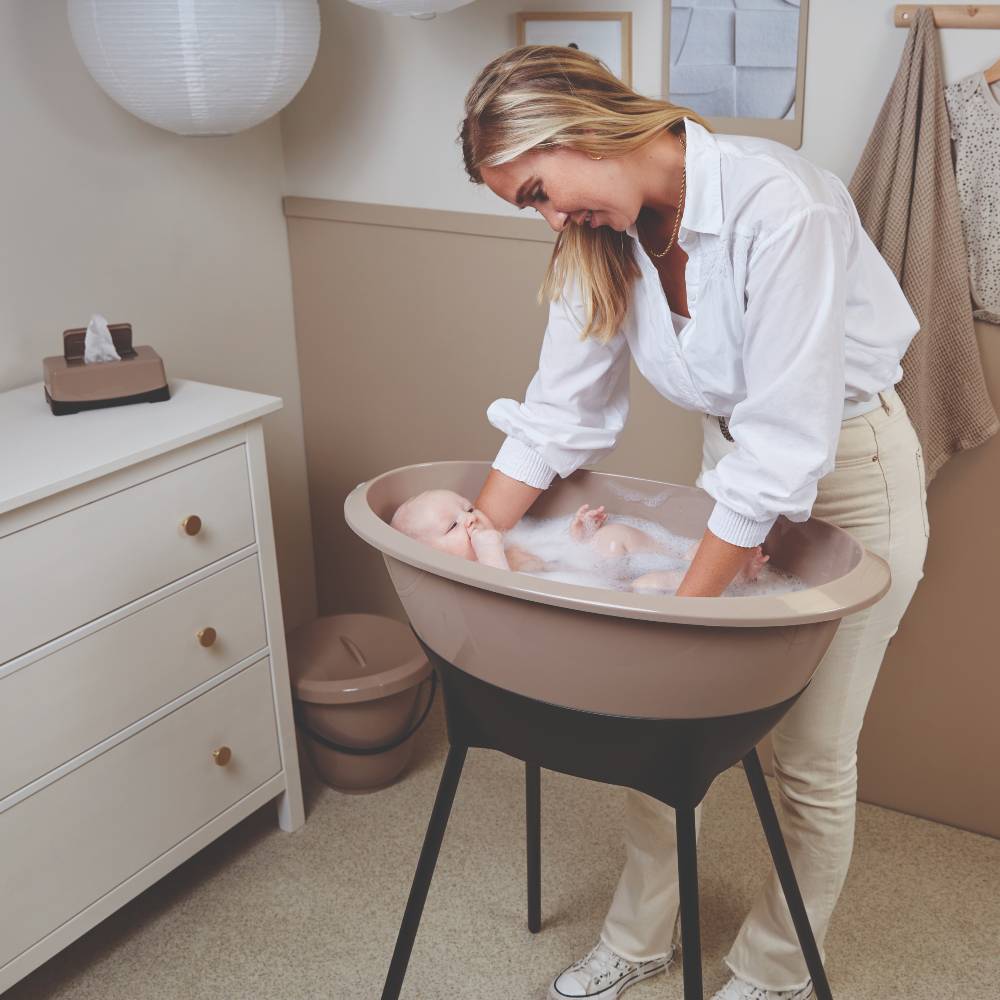Woman bathing baby in a LUMA baby bath, sitting on a LUMA baby bath stand. 