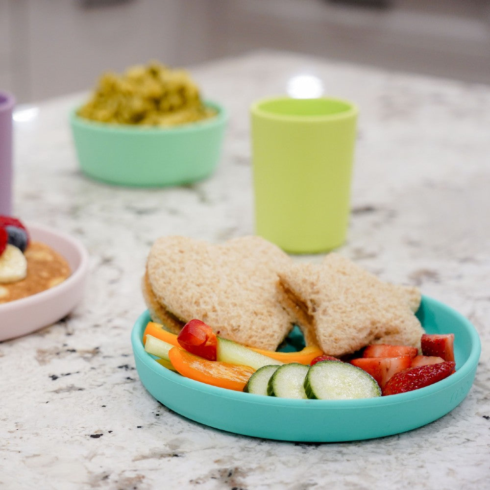 Children's lMelii silicone unch with sandwiches, fruits, and vegetables on a marble surface.