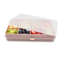 Pink bento box with compartments filled with fruits on a white background