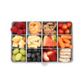 Assorted healthy snacks including fruits and vegetables in a compartmentalized container on a white background.