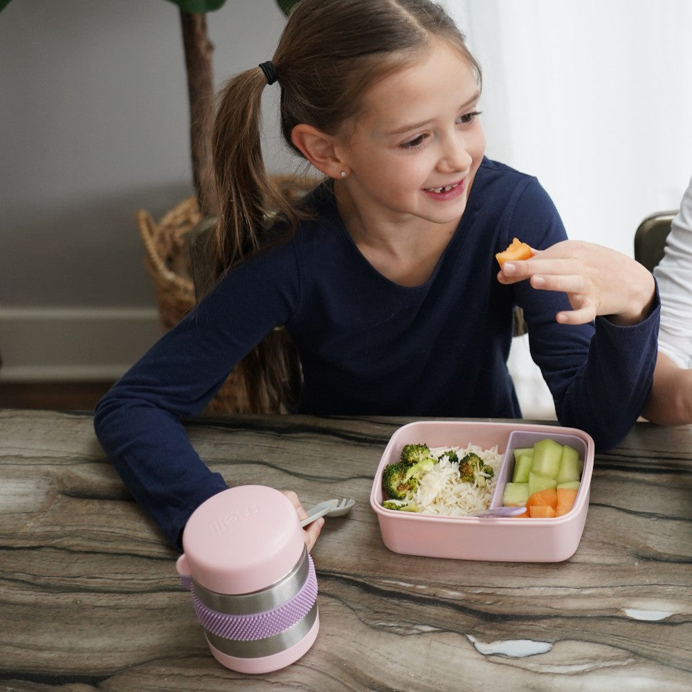 Insulated food jar for children with a lid and spoon with a child eating their lunch on a wood table