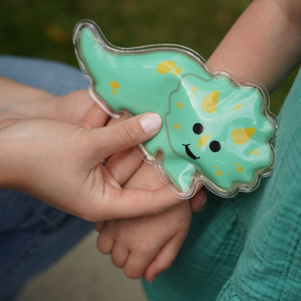 Person holding a green dinosaur-shaped cookie with a smiley face.