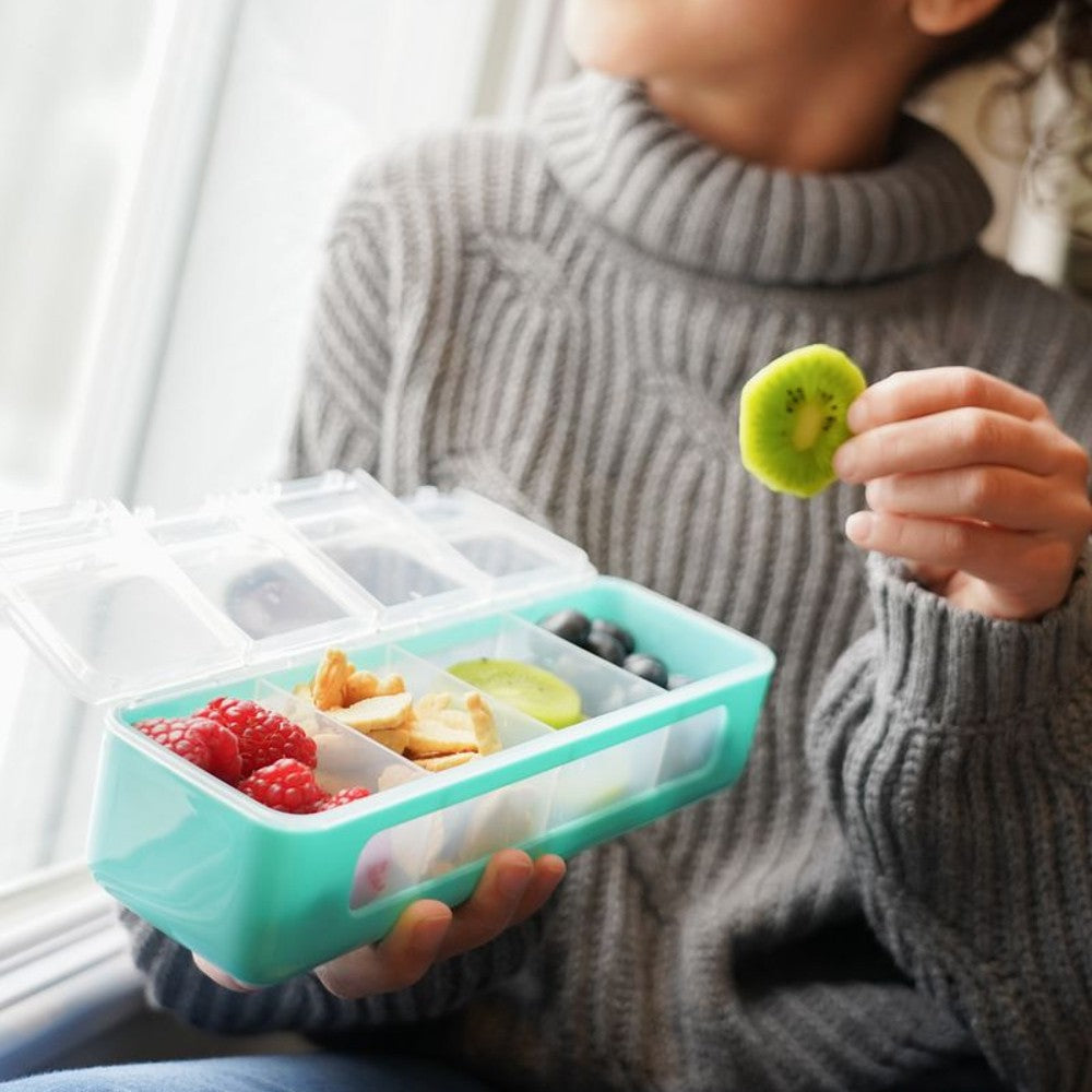 Person holding a teal mrelii snackle bento box with food and a kiwi slice.