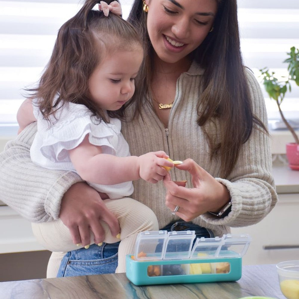 Woman and child interacting with a colorful compartmentalized container on a table.