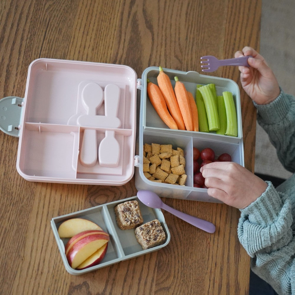 Melii Bento box with compartments of fruits, vegetables, and snacks on a wooden table.