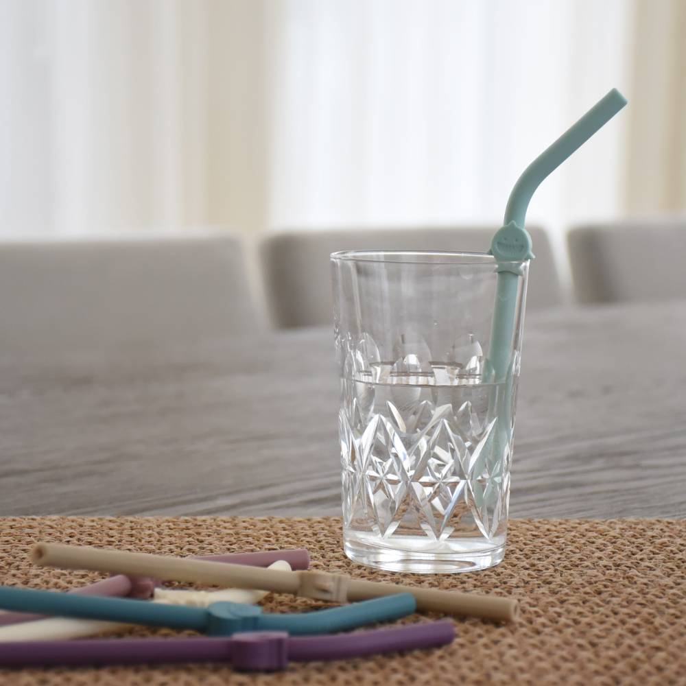 Clear glass with a green straw on a textured surface, with other straws in the foreground.