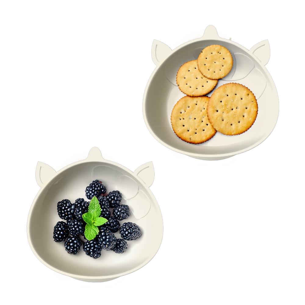 Two unicorn-shaped bowls with one containing blackberries and the other with crackers on a white background.