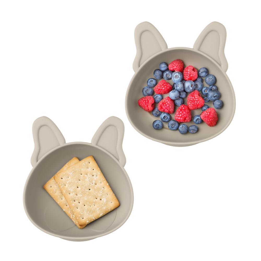 Two dog-shaped suction bowls with crackers and berries on a white background