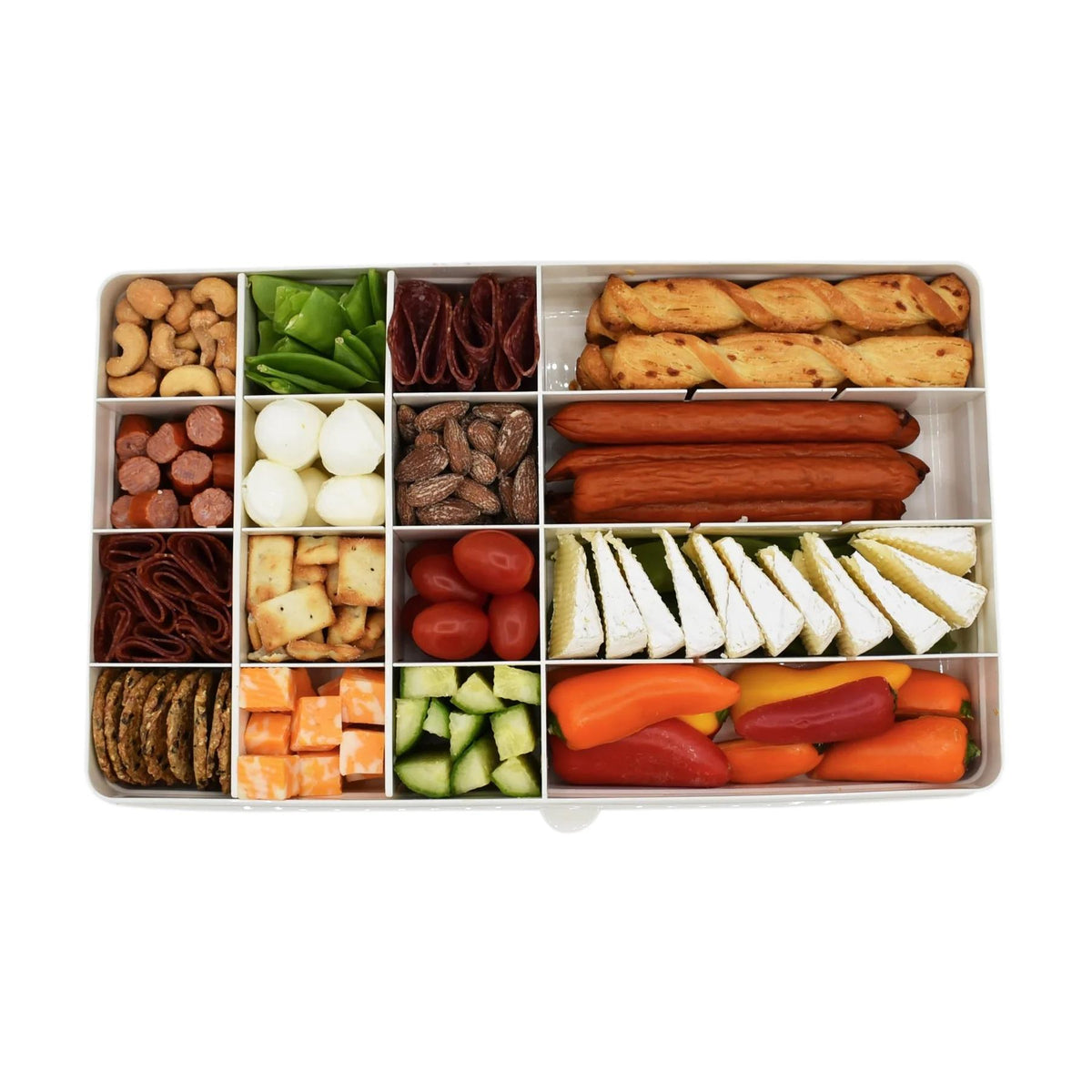 Assorted snacks including fruits, vegetables, and meats in a compartmentalized container on a white background