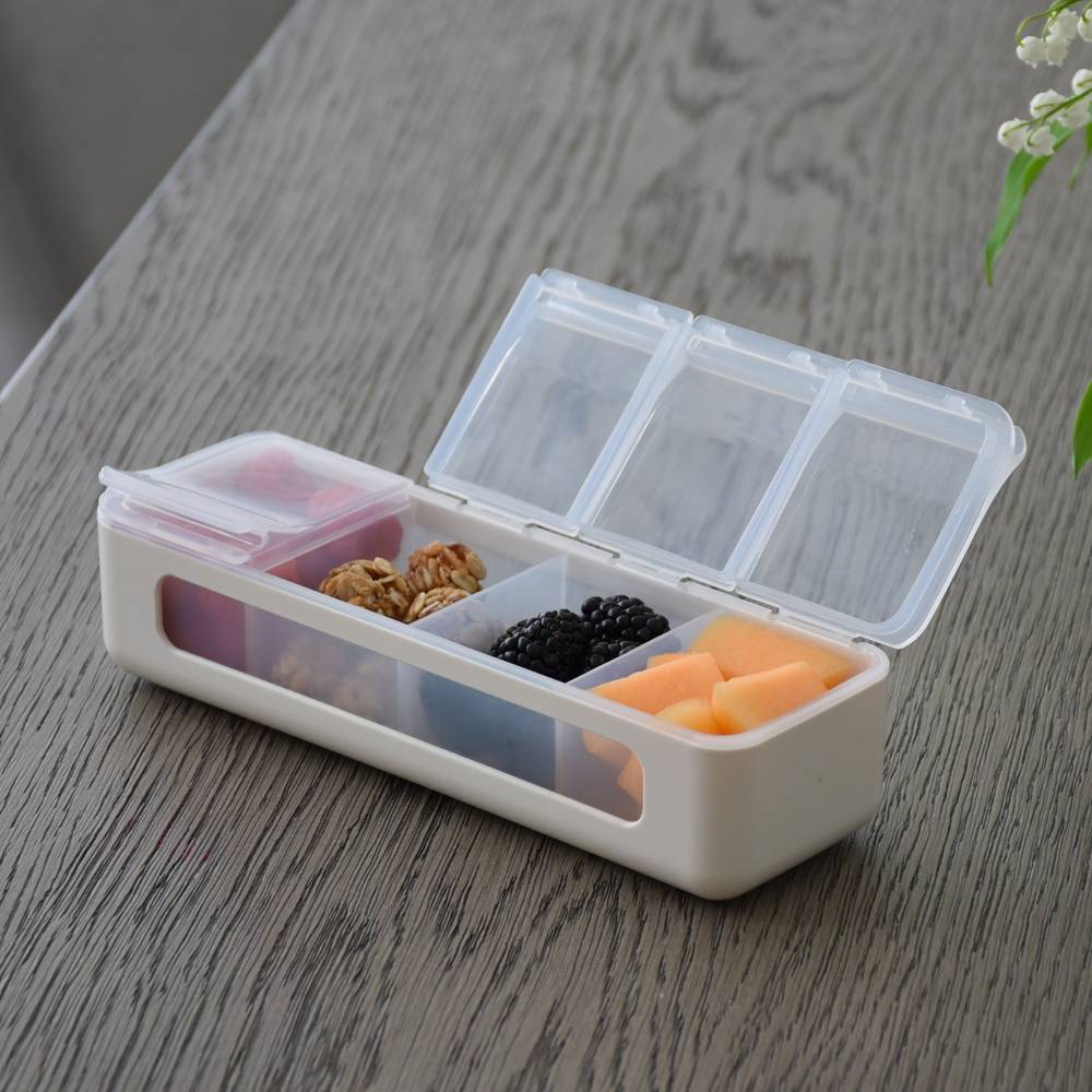 Transparent compartmentalized container with snacks on a wooden surface