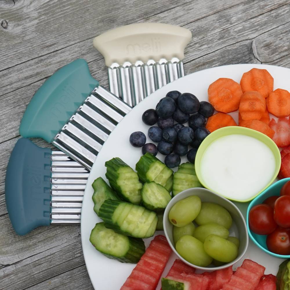 Assorted fruits and vegetables on a plate with two kitchen scrub brushes on a wooden surface.