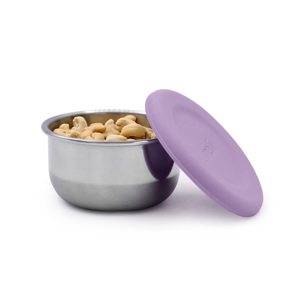 Stainless steel snack container with purple lid filled with cashews on a white background