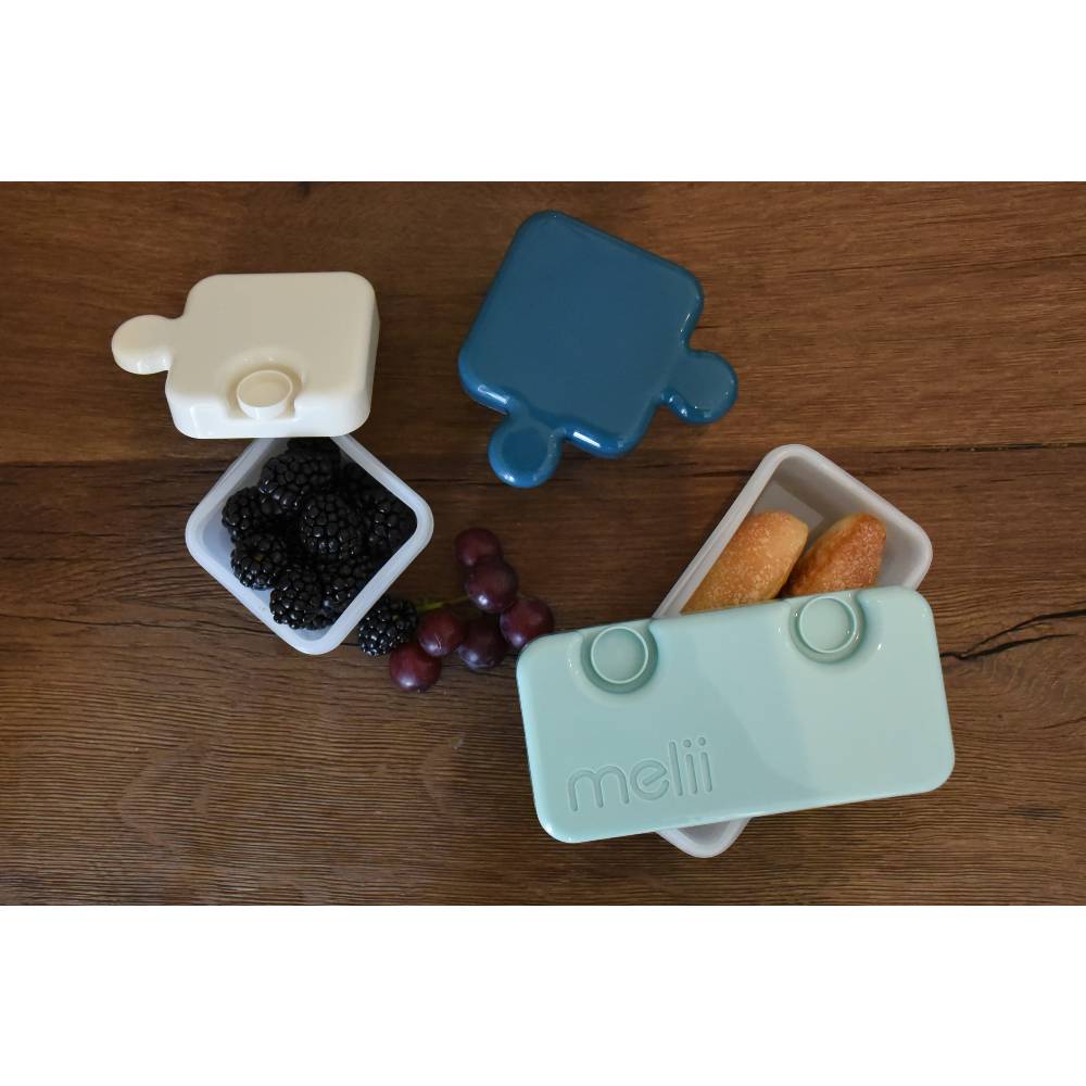 Three puzzle shaped bento box pieces with berries and bread.