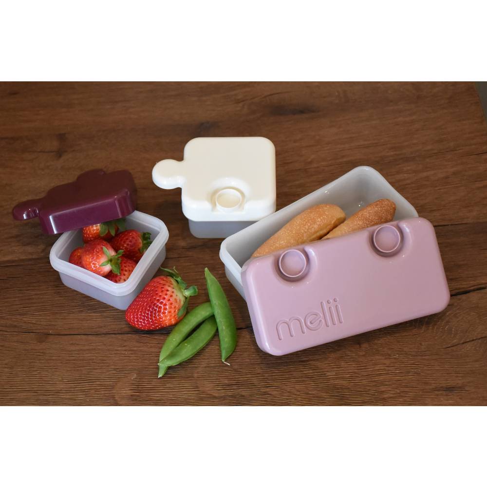 Set of three small containers with food on a wooden surface, featuring the brand 'mellii'.