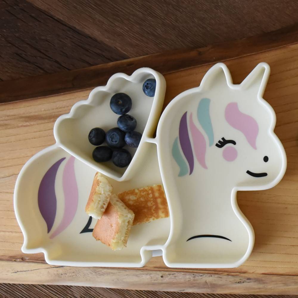 Unicorn-shaped plate with compartments containing blueberries and bread on a wooden surface
