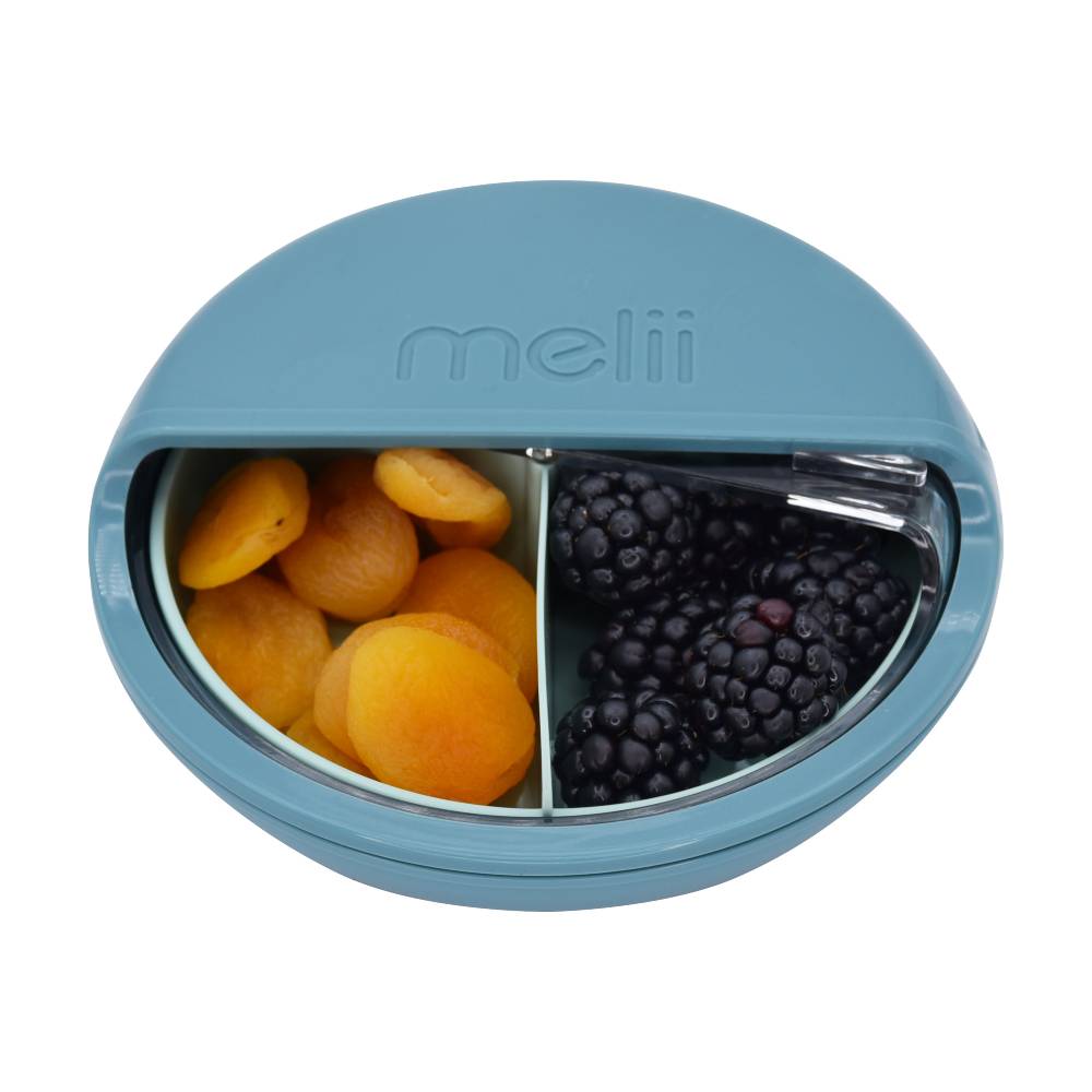 Blue bento box with compartments filled with apricots and blackberries on a white background