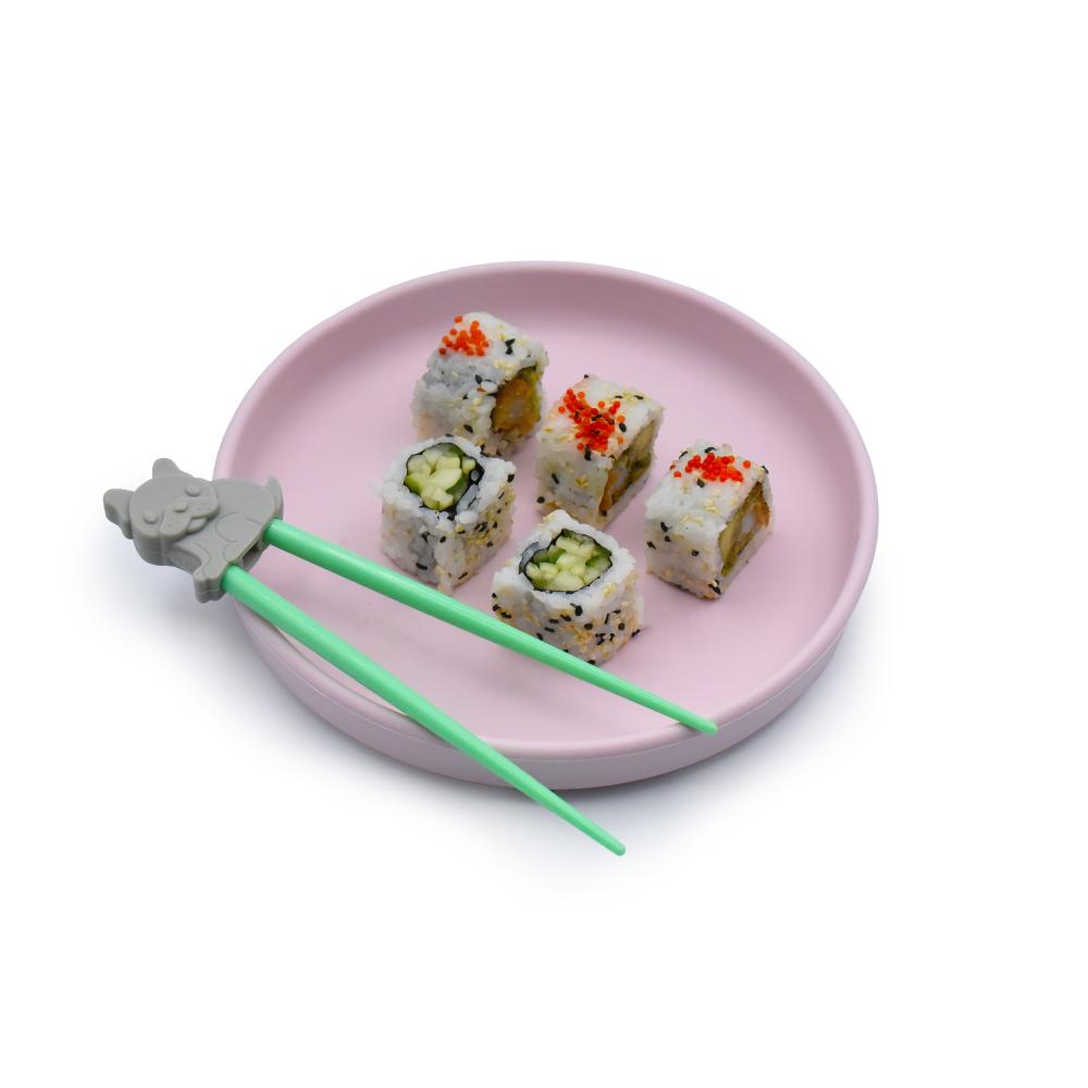 Pink plate with sushi rolls and green kids learner chopsticks on a white background