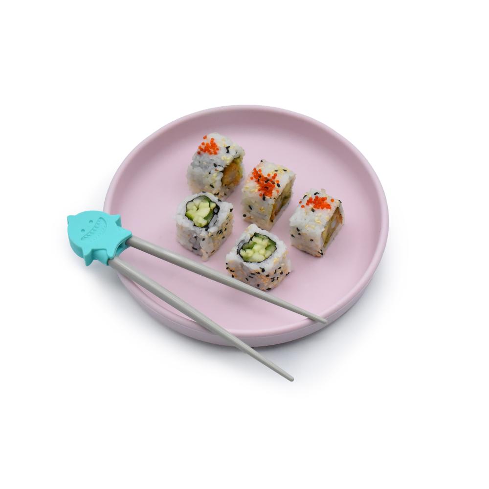Sushi pieces on a pink plate with a pair of kids easy to use learning chopsticks featuring a turquoise holder.