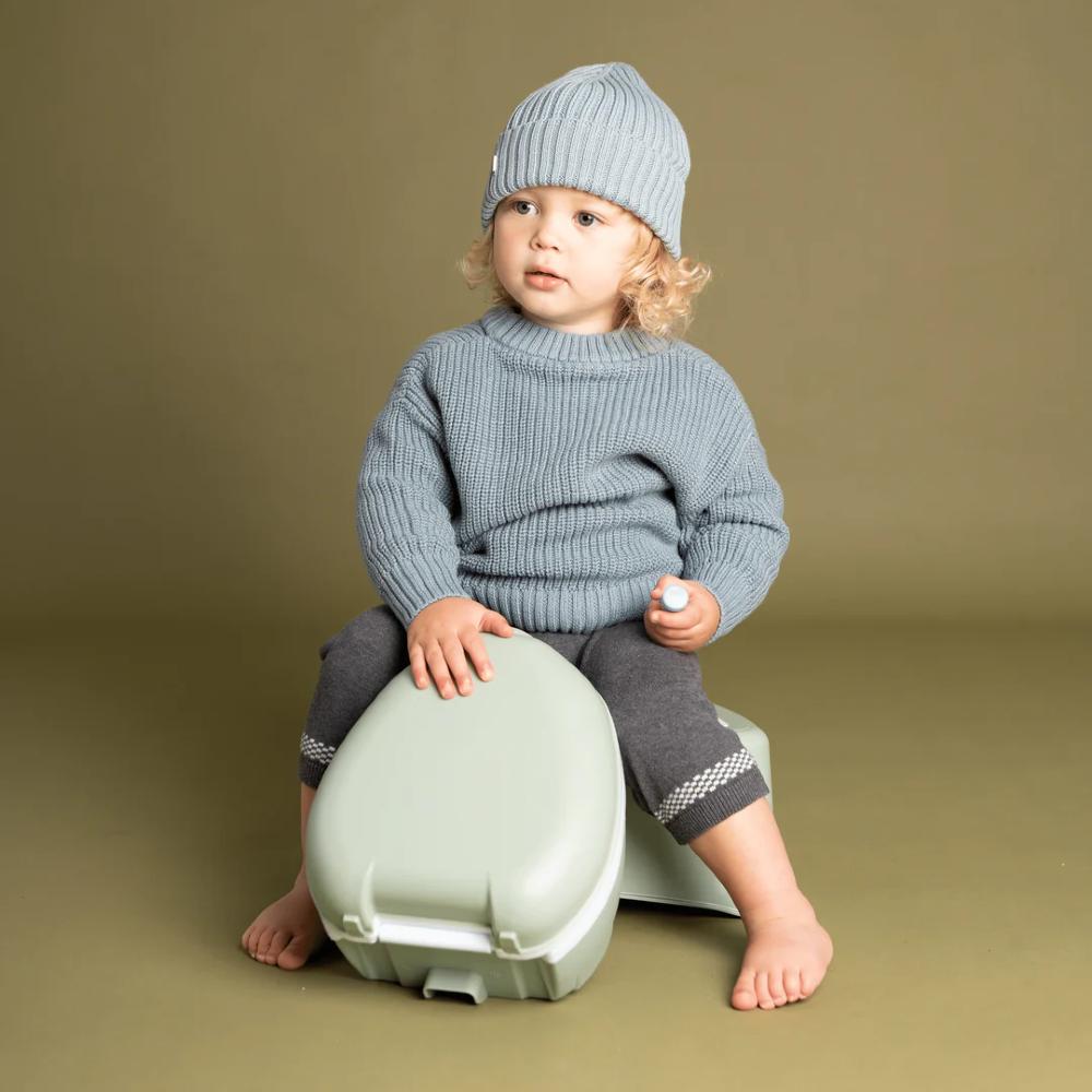 Baby holding My Carry Potty against green background.