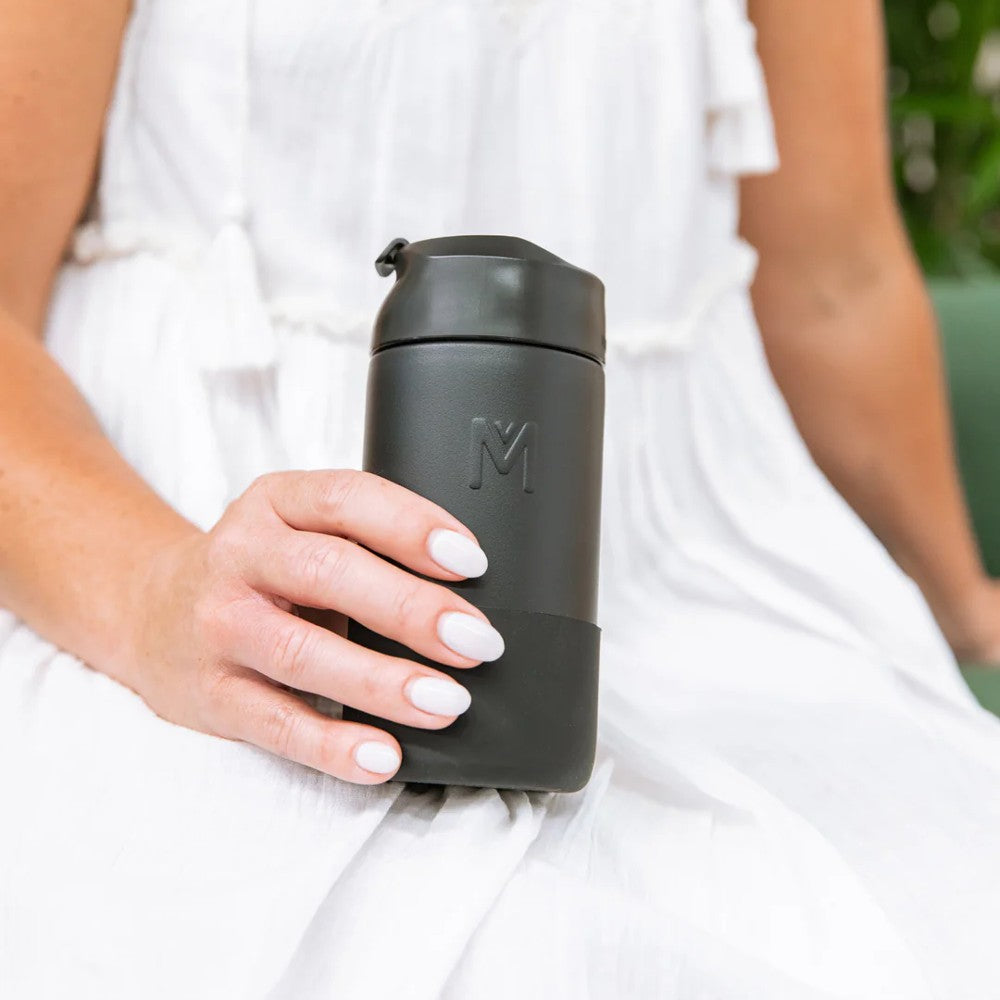 A hand holding a black montii fusion coffee cup. 