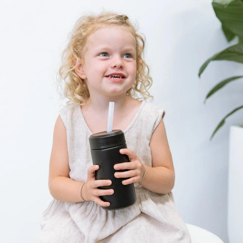 A child holding a black montii fusion smoothie cup with a stainless steel straw. 