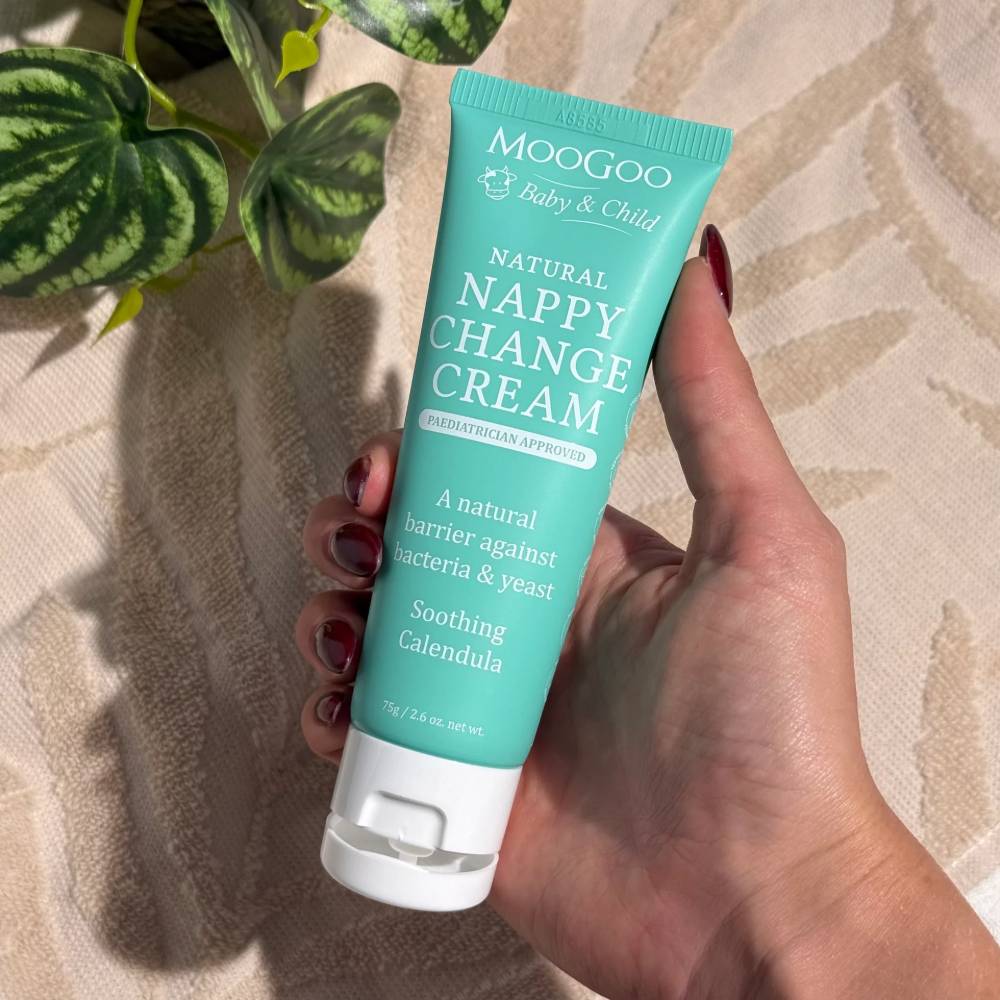 Hand holding a tube of Moogoo Natural Nappy Change Cream against a neutral background