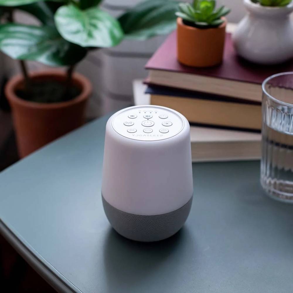 Yogasleep White Noise machine on a table with books and plants in the background