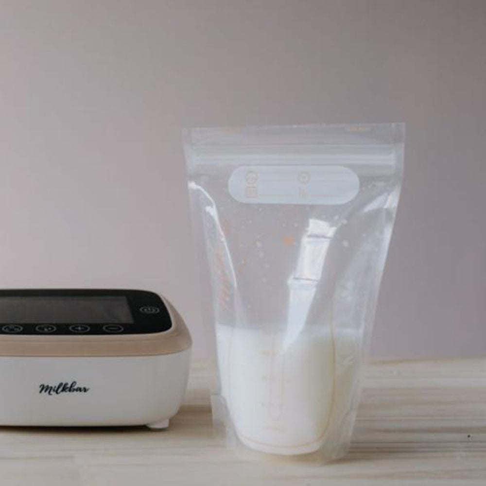 Milkbar breast pump with a filled milk storage bag on a light surface.