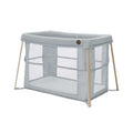 A light gray baby travel cot with a light wood frame and mesh sides, shown on a plain white background.