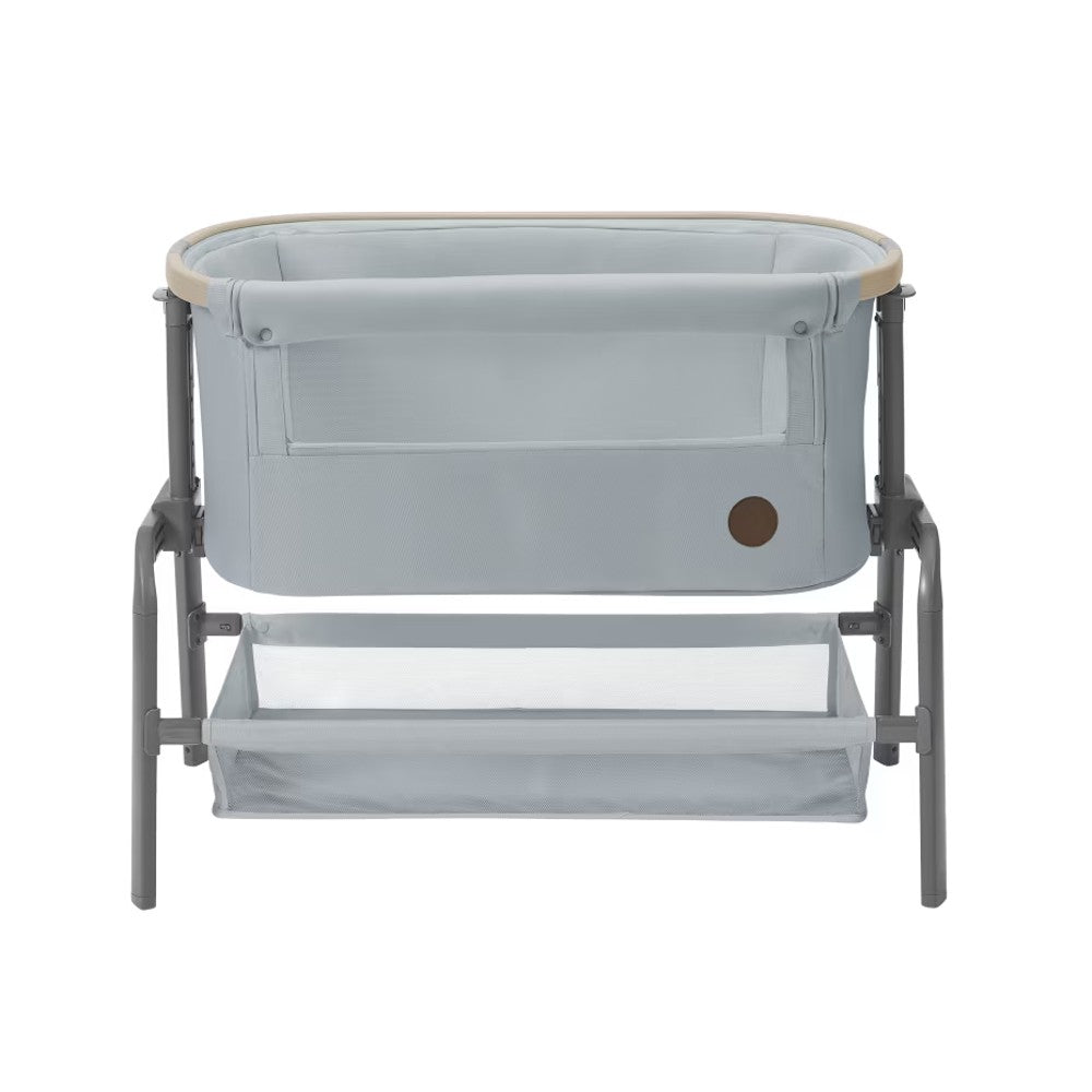 A light gray baby bassinet with a matching metal frame and changing tray, featuring a natural wood-look trim along the top edge and a small circular brown logo on the front.