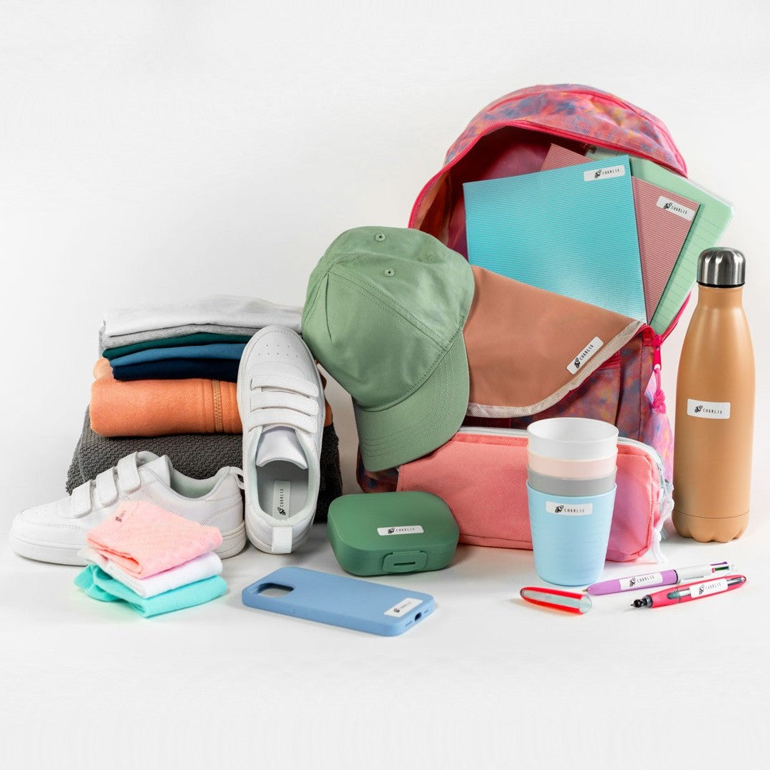 Backpack with colorful labelled items including a cap, shoes, and stationery on a white background