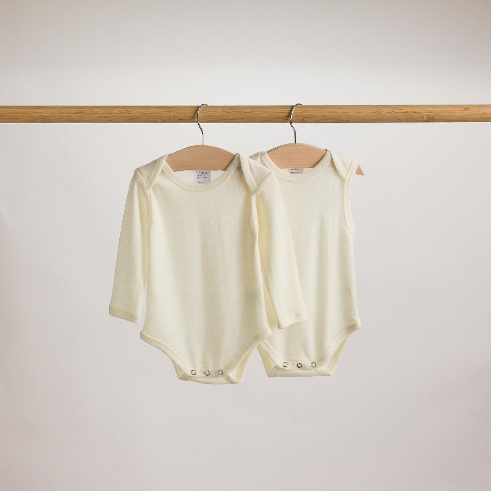 Two baby rompers hanging on a wooden rod against a plain background