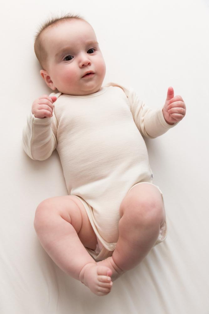 A baby lying on a white blanket, wearing a light cream long-sleeve deluxe merino bodysuit
