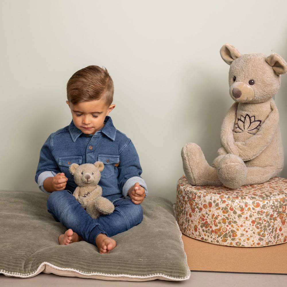 A boy sitting down holding a mindful bear, meditating next to a huge happy horse mindful bear. 