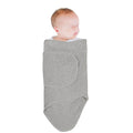 Newborn baby wrapped in a grey miracle blanket swaddle on a white background