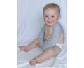 Baby wearing grey mitten sleeves against white background.